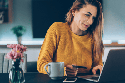 Young woman paying online with credit card and laptop at home, as ecommerce continues to top retail competition.