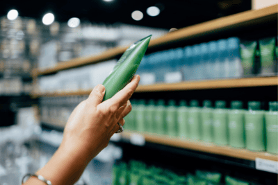 A cropped photo of a white woman holding a tube of a hand cream while shopping at a physical store that has worked on product assortment to beat out its retail competition.