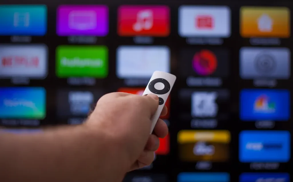 Hand with Apple TV remote, pointing toward TV with all the streaming apps on display